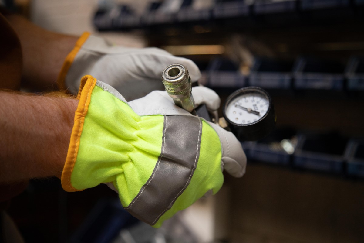 worker wearing high-visibility work gloves and holding pressure gauge