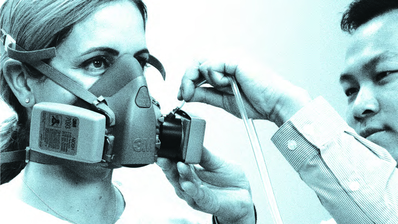 man placing hose on woman's respirator for her fit test