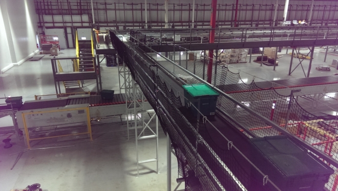 boxes moving on an elevated conveyor belt in a warehouse with debris netting protecting the sides