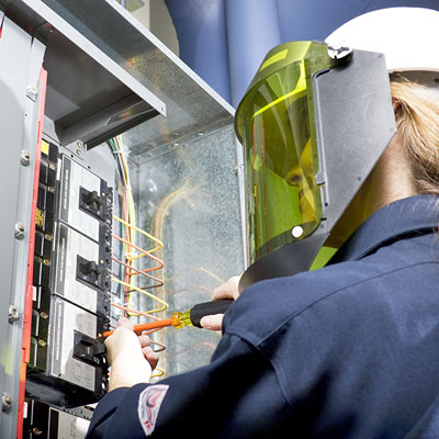 Female safety worker working on an electrical panel with arc Flash mask