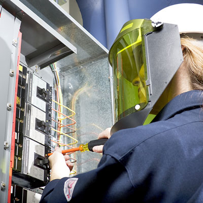 Female safety worker working on an electrical panel with arc Flash mask